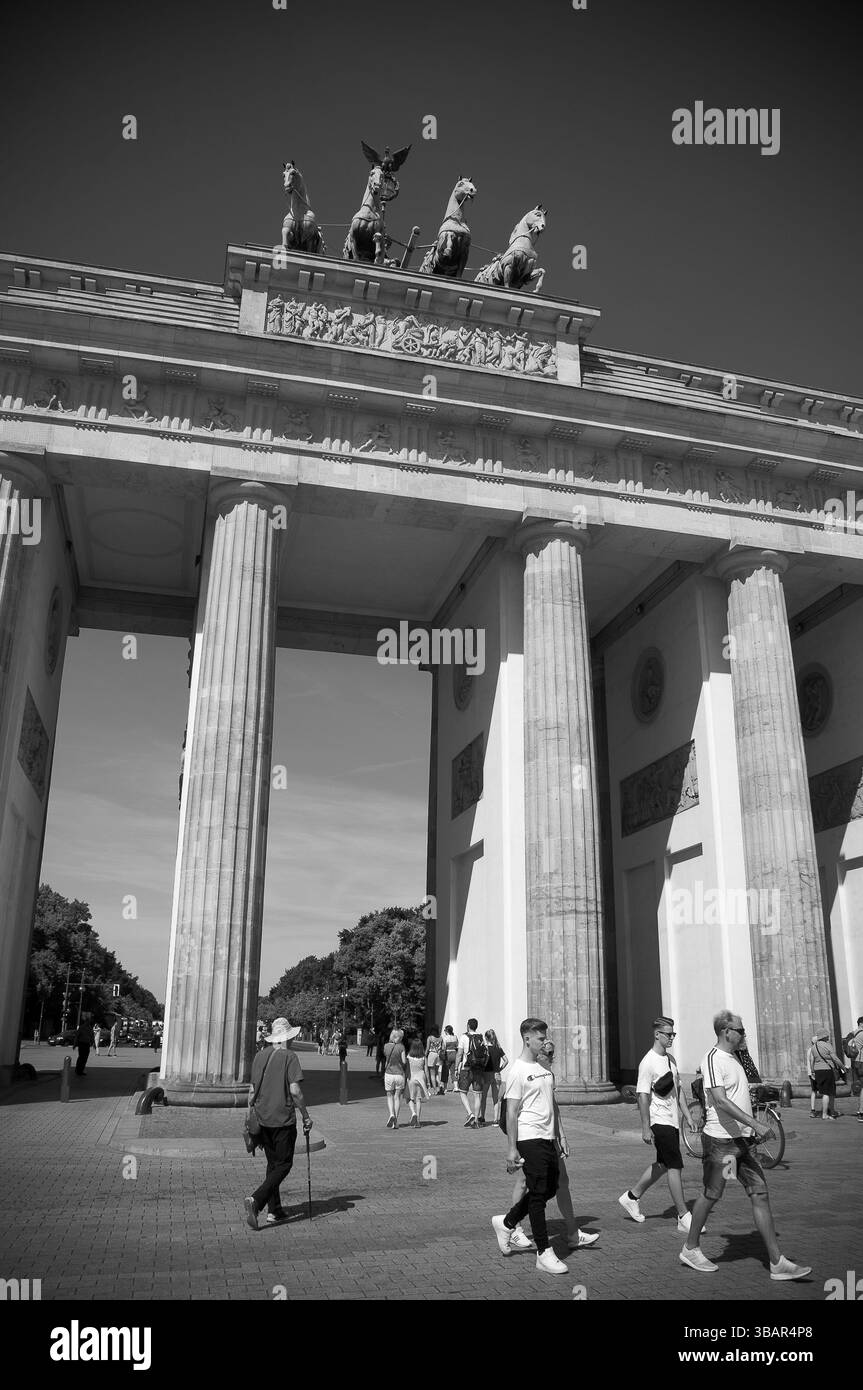 Gruppi di turisti camminano sotto l'iconica porta di Brandeburgo a Berlino, mostrando l'architettura storica sotto la luce del giorno. Foto Stock