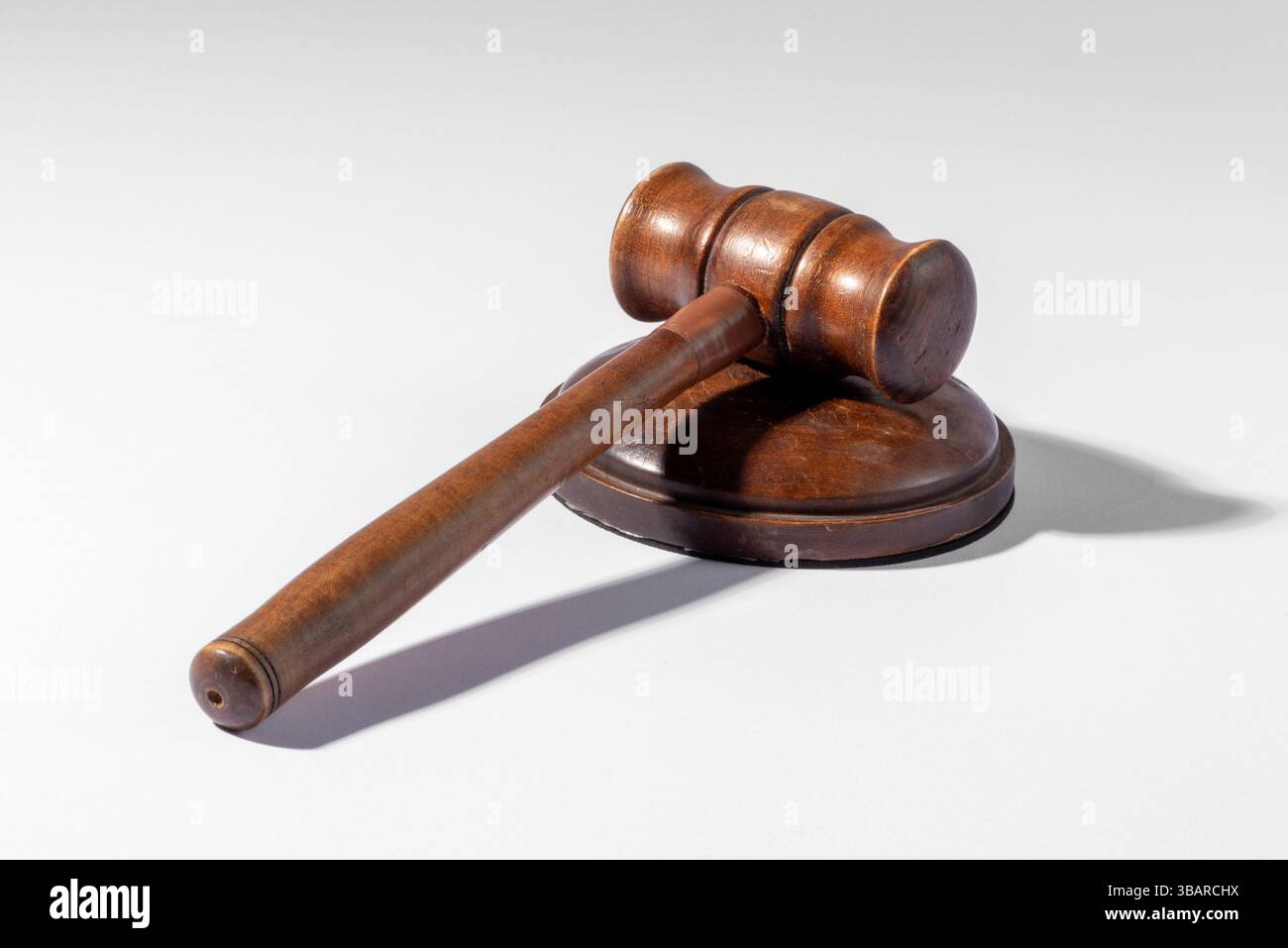 Martelletto di legno appoggiato su un blocco sonoro su un semplice sfondo bianco, che rappresenta la legge, la giustizia e i procedimenti giudiziari Foto Stock