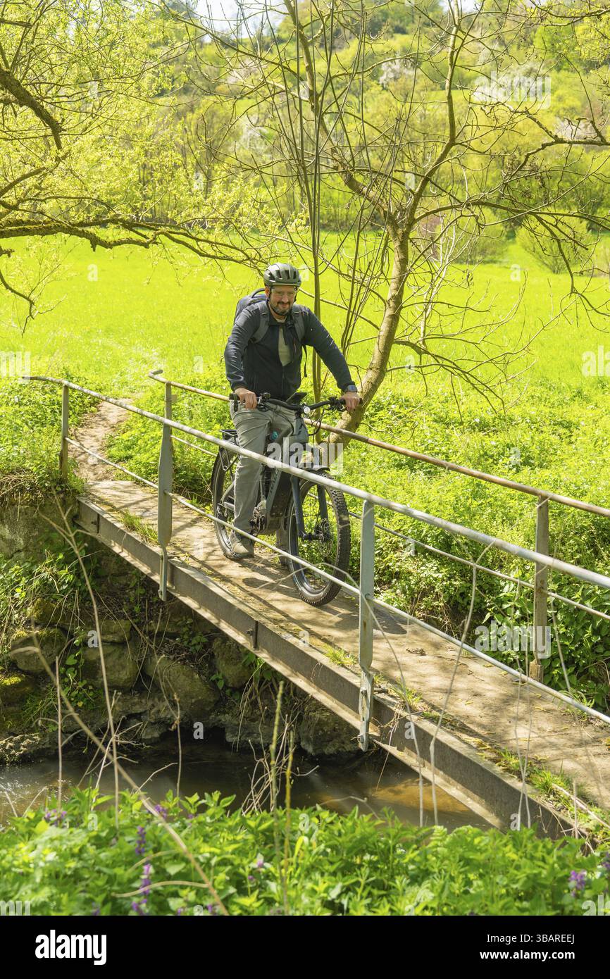 Un ciclista sorridente attraversa un ponte in un verde paesaggio primaverile, Gechingen, distretto di Calw, Germania, Europa Foto Stock