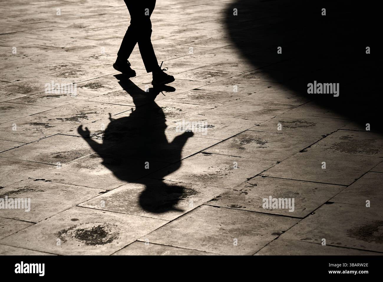 Silhouette di una persona che cammina con una mano gestante, che getta un'ombra spettacolare sulle piastrelle di pietra. Foto Stock Silhouette di una persona che cammina con una mano gestante, che getta un'ombra spettacolare sulle piastrelle di pietra. Foto Stock