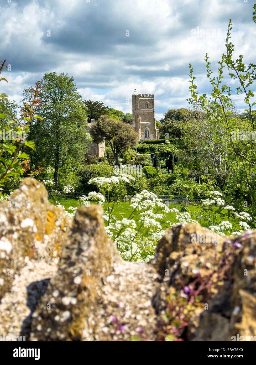 St Nicholas Church, Abbotsbury, Dorset, Regno Unito, visto attraverso un muro di pietra secca. La prima costruzione risale al XIV e XV secolo e questo Foto Stock