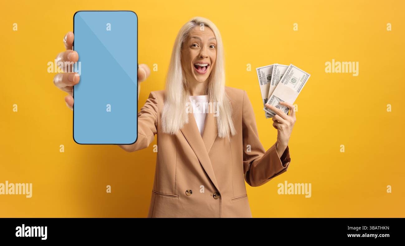 Giovane donna felice con soldi e smartphone con schermo blu su sfondo giallo Foto Stock