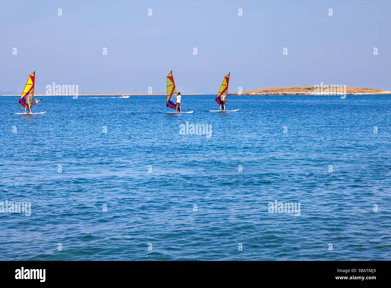 Premantura, Croazia - 22 agosto 2024: Tre uomini frequentano una scuola di windsurf a Capo Kamenjak, vicino a Premantura in Istria, Croazia. La scena captur Foto Stock