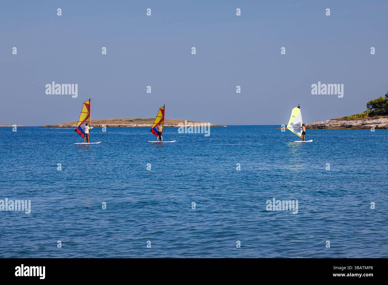 Premantura, Croazia - 22 agosto 2024: Tre uomini frequentano una scuola di windsurf a Capo Kamenjak, vicino a Premantura in Istria, Croazia. La scena captur Foto Stock
