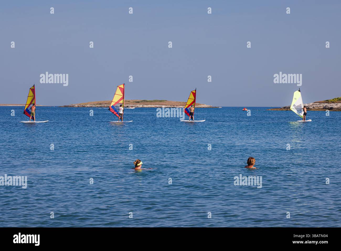 Premantura, Croazia - 22 agosto 2024: Tre uomini frequentano una scuola di windsurf a Capo Kamenjak, vicino a Premantura in Istria, Croazia. La scena captur Foto Stock