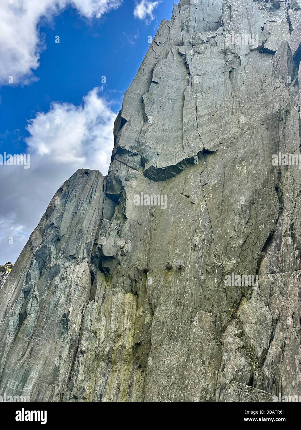 La scogliera in ardesia testurizzata della cava Dinorwic nel Galles del Nord, sotto un cielo blu brillante con soffici nuvole bianche. Storico paesaggio minerario di ardesia. - Immagine stock catturata con smartphone