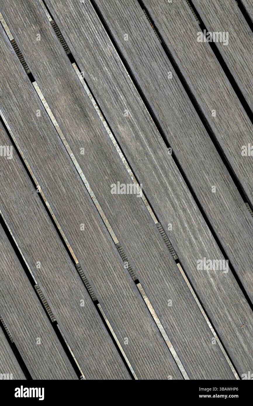 Primo piano di tavole in legno grigio invecchiato disposte diagonalmente con spazi ristretti su una base in calcestruzzo. Struttura a grana visibile. Ideale per gli sfondi Foto Stock