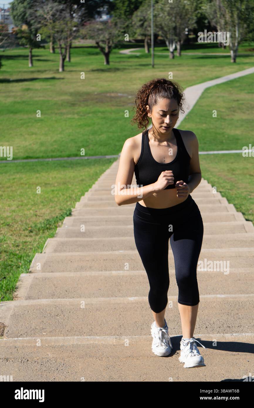 Sportiva concentrata che corre sulle scale durante la sua routine di allenamento in un parco Foto Stock