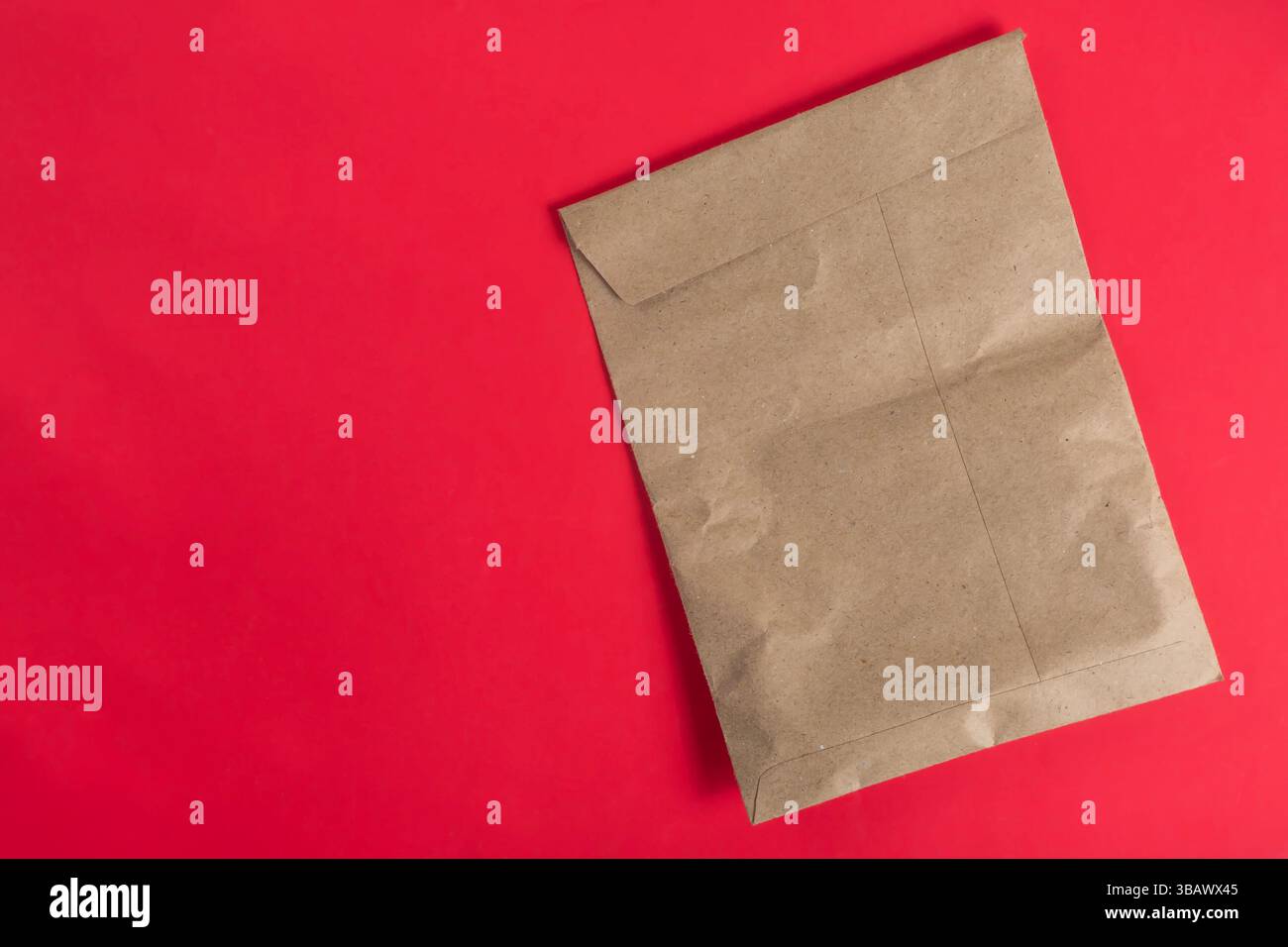 Un sacchetto di carta marrone posizionato su un vivace sfondo rosso che simboleggia idee ecologiche e minimalismo. Foto Stock