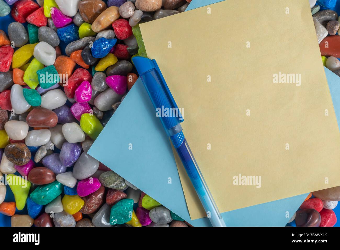 Una vivace composizione di ciottoli colorati, carta gialla e blu e una penna. Perfetto per progetti artistici o didattici. Foto Stock