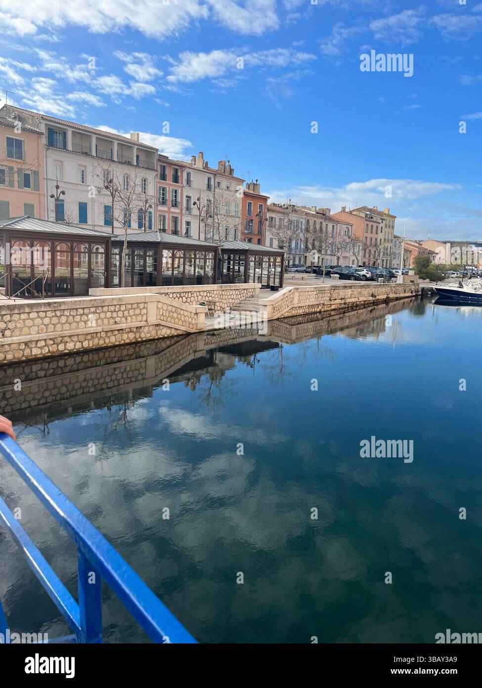 Case colorate e edifici sul canale si riflettono in acque calme in una tranquilla città francese sotto un cielo limpido. - Immagine stock catturata con smartphone