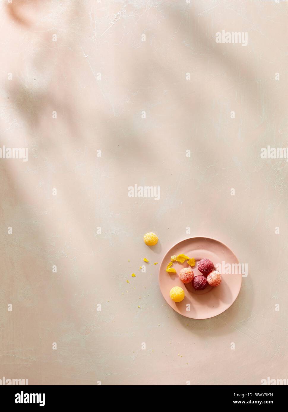 Caramelle rotonde colorate su piatto rosa con luce d'ombra morbida Foto Stock