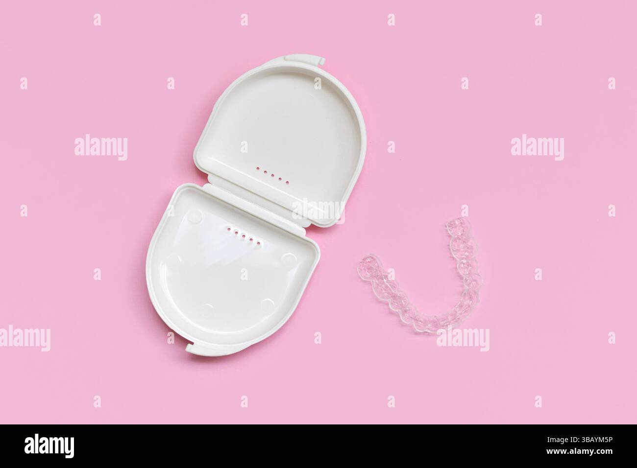 Vista dall'alto della protezione dentaria trasparente personalizzata allineatori trasparenti per la parte inferiore della ganascia con custodia bianca su sfondo rosa Foto Stock