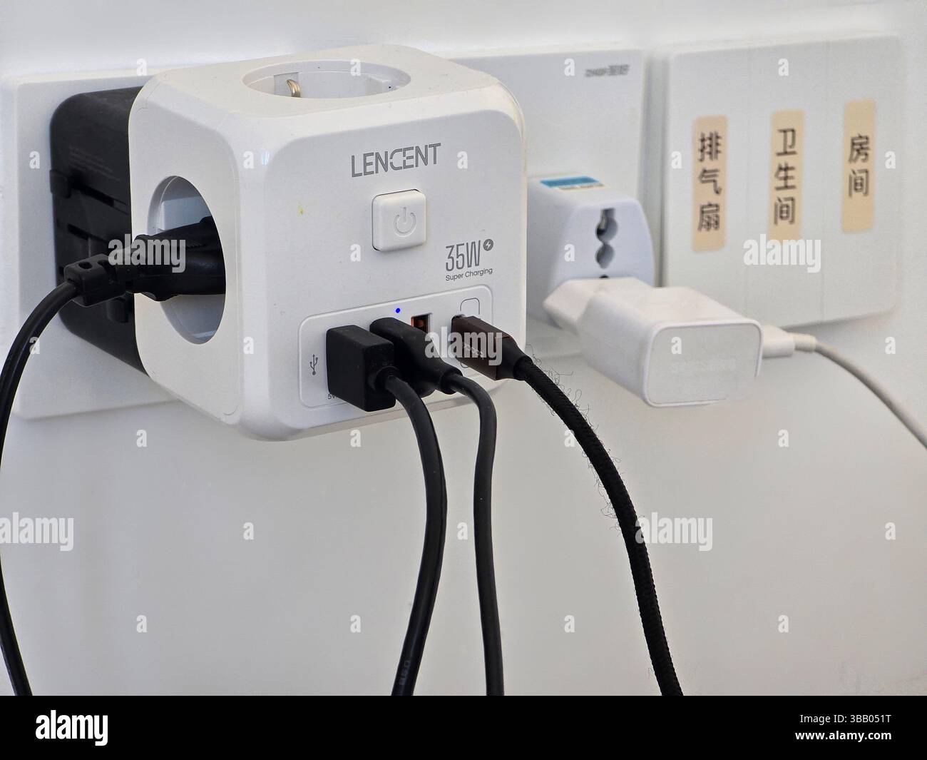 Più adattatori USB e spina collegati a un hub di alimentazione LENCT montato su una presa a muro in un moderno bagno cinese o in un ambiente abitativo. Foto Stock