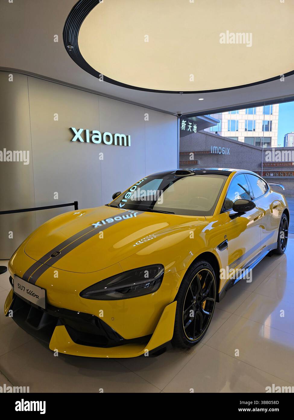 Vista laterale di un'auto Xiaomi SU7 gialla e riflessi di un'altra EV all'interno di un moderno showroom con luce circolare in Cina. Foto Stock