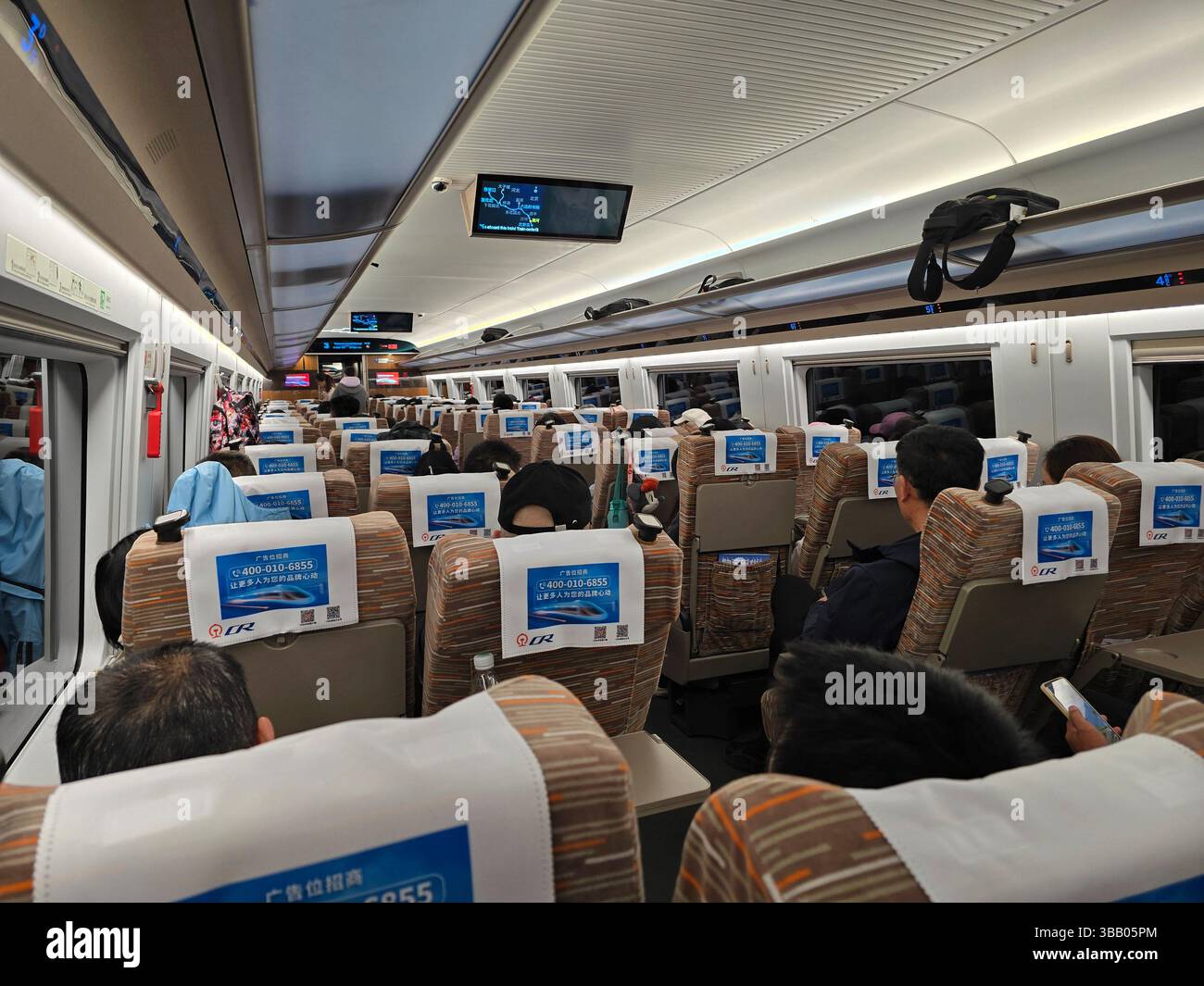 Passeggeri seduti all'interno di un treno cinese ad alta velocità con schermi sospesi e posti accanto al finestrino durante il viaggio. Foto Stock