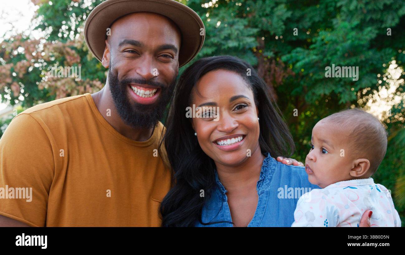 Sorridente famiglia afroamericana coccolare e giocare con Baby Daughter in Garden at Home Foto Stock