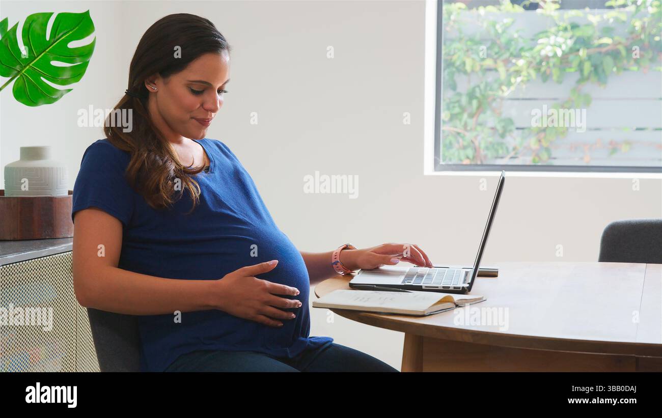 Donna incinta che usa il laptop al tavolo che lavora da casa Foto Stock