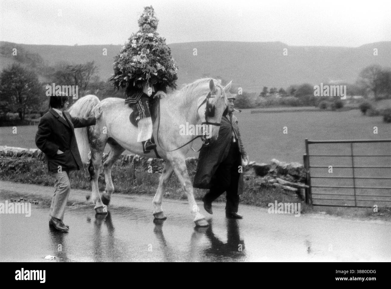 Castleton Garland Day Oak Apple Day Derbyshire Regno Unito. Il re a cavallo con due membri del comitato che guidano il suo cavallo alla testa di una processione intorno ai confini della parrocchia. Si trova sotto una ghirlanda di fiori a forma di alveare che verrà posta alla fine della giornata sulla torre della chiesa. Castleton, Derbyshire, Inghilterra 1972 1970s HOMER SYKES Foto Stock