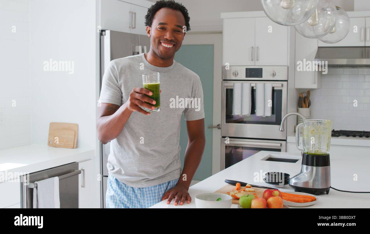 Ritratto dell'uomo che indossa pigiami in cucina e beve frullato di frutta e verdura appena fatto Foto Stock