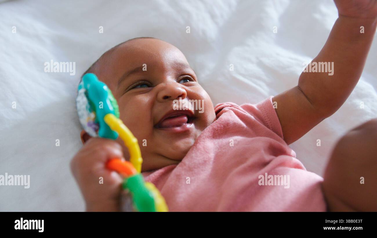 Primo piano di una bambina sorridente sdraiata sul letto dei genitori a casa che gioca con il giocattolo Foto Stock