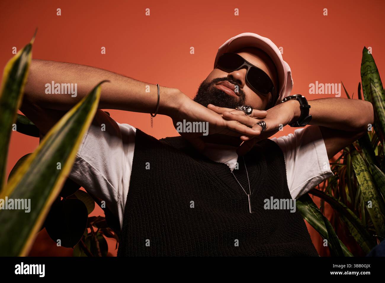 Un giovane uomo alla moda si rilassa tranquillamente tra la vegetazione lussureggiante, immergendosi nell'estetica estiva. Foto Stock