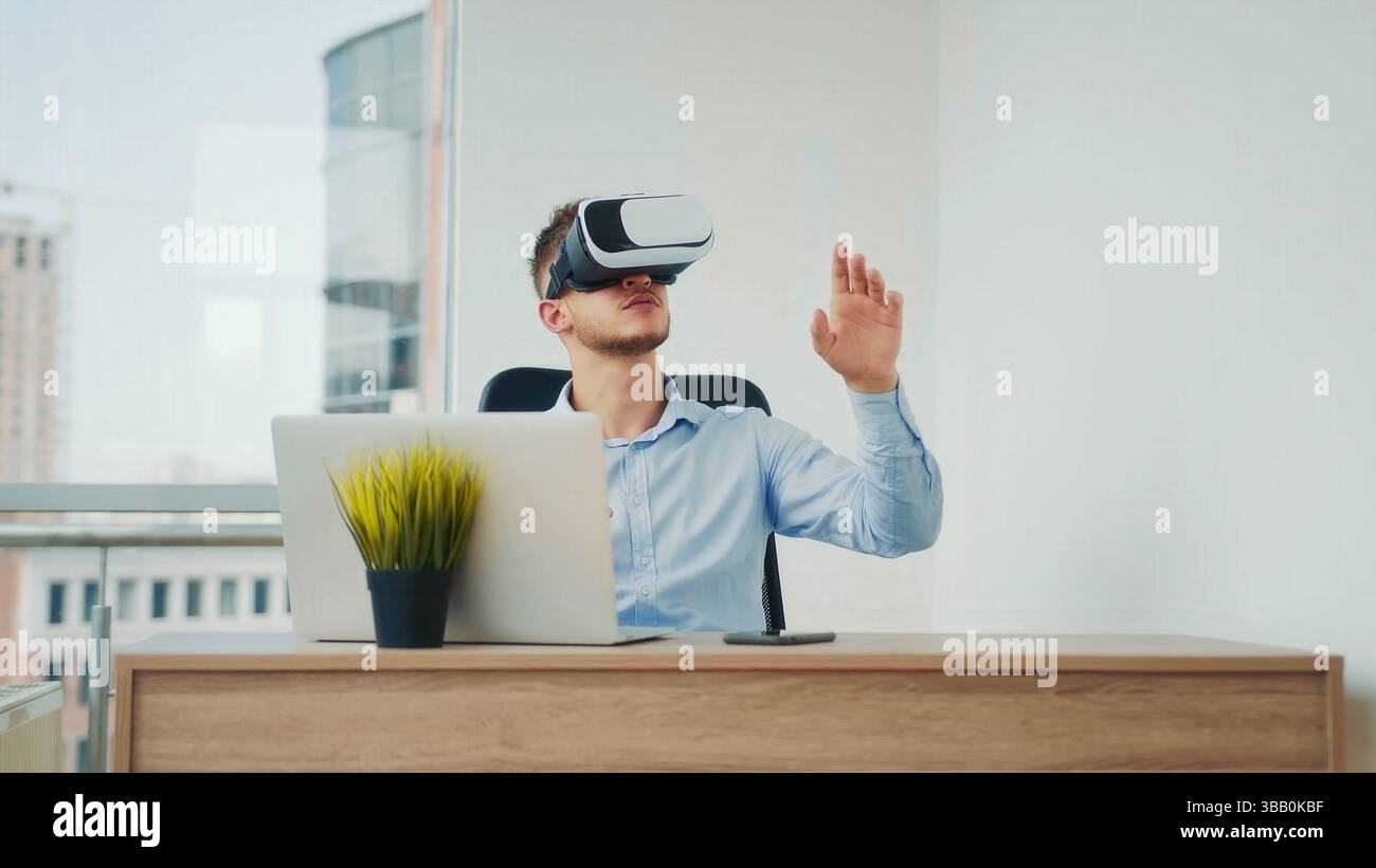 Uomo che usa il visore VR in un ufficio moderno. Un giovane uomo seduto a una scrivania in un ufficio luminoso, che indossa un visore per la realtà virtuale mentre interagisce con il Foto Stock