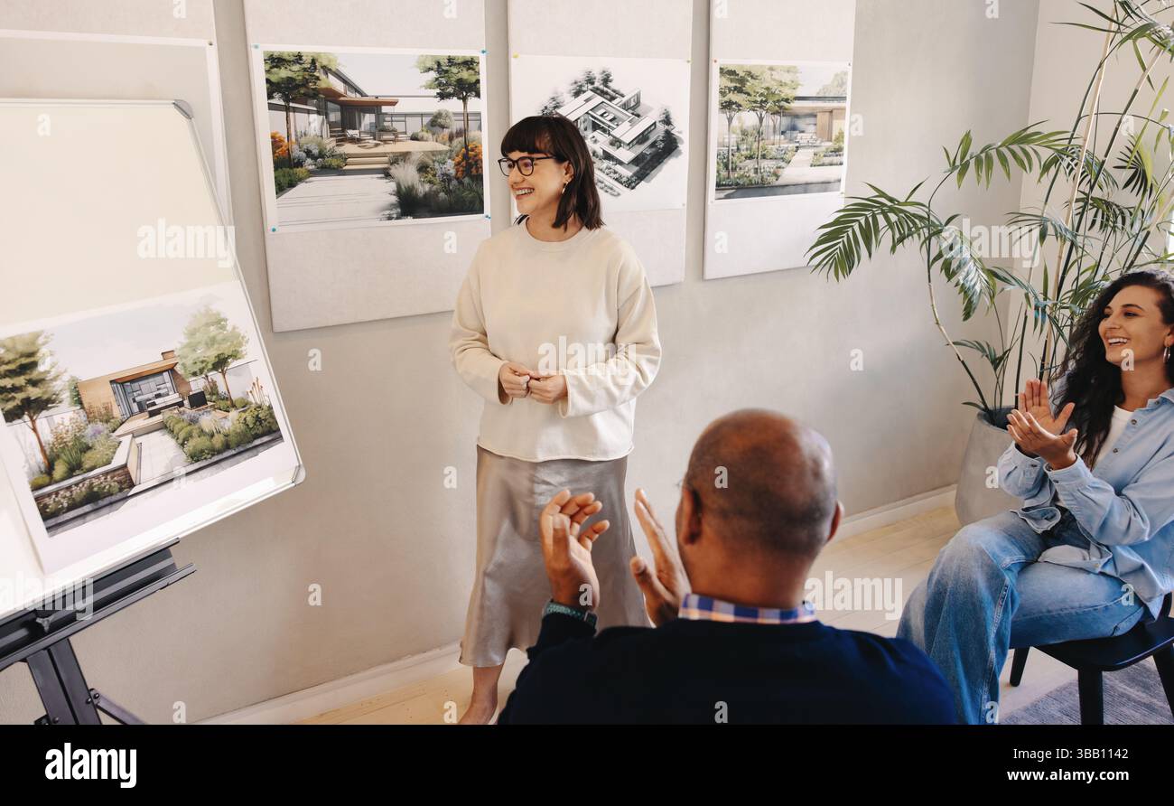 I colleghi si sono riuniti in un ambiente professionale, presentando un progetto architettonico e apprezzando il feedback. L'ambiente collaborativo mette in evidenza Foto Stock