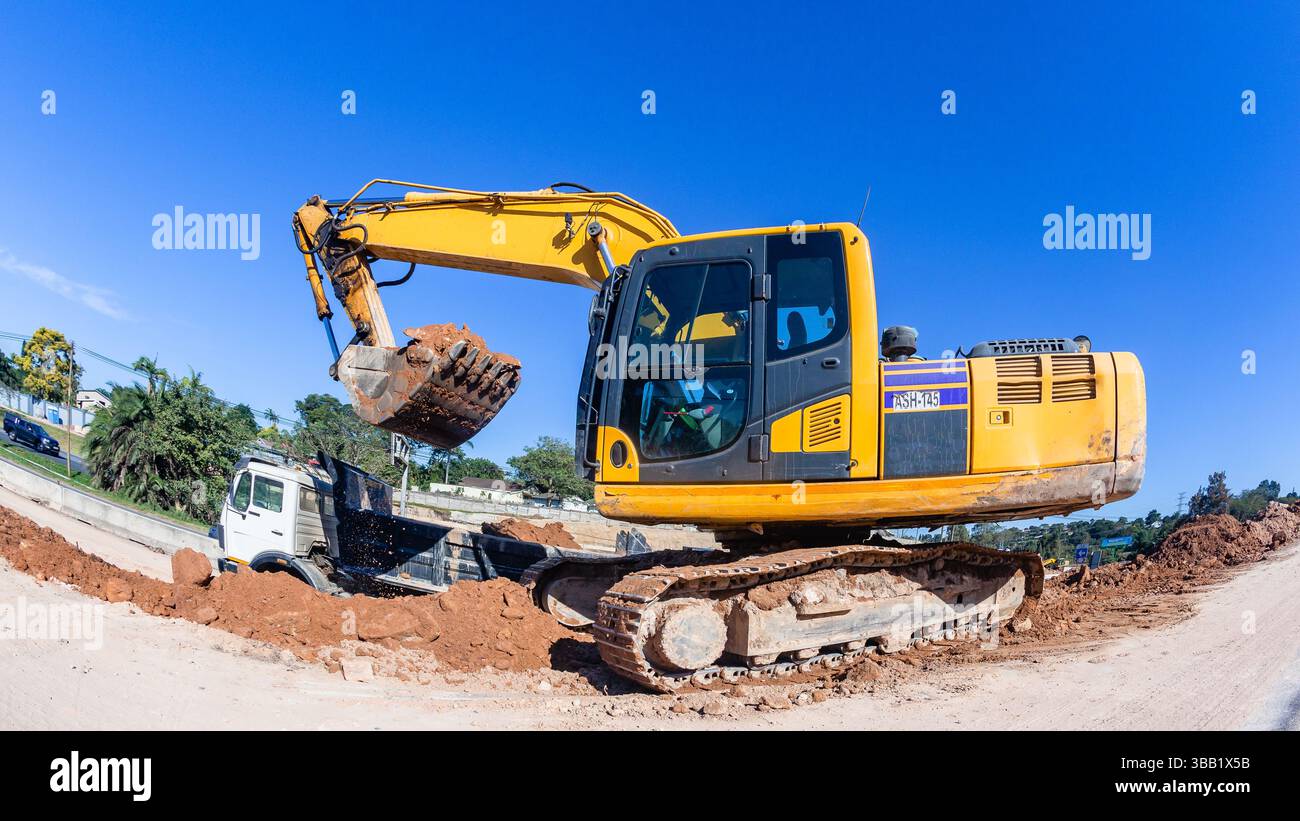 Costruzione industriale espansione stradale escavatore pesante ribaltamento della sabbia di terra nel dumper in una giornata di cielo azzurro. Foto Stock