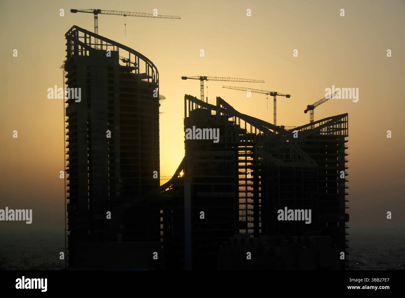 Costruzione di un nuovo edificio. Molte gru a grappolo e attrezzature per l'edilizia industriale contro il sole. silhouette gru edifici Foto Stock