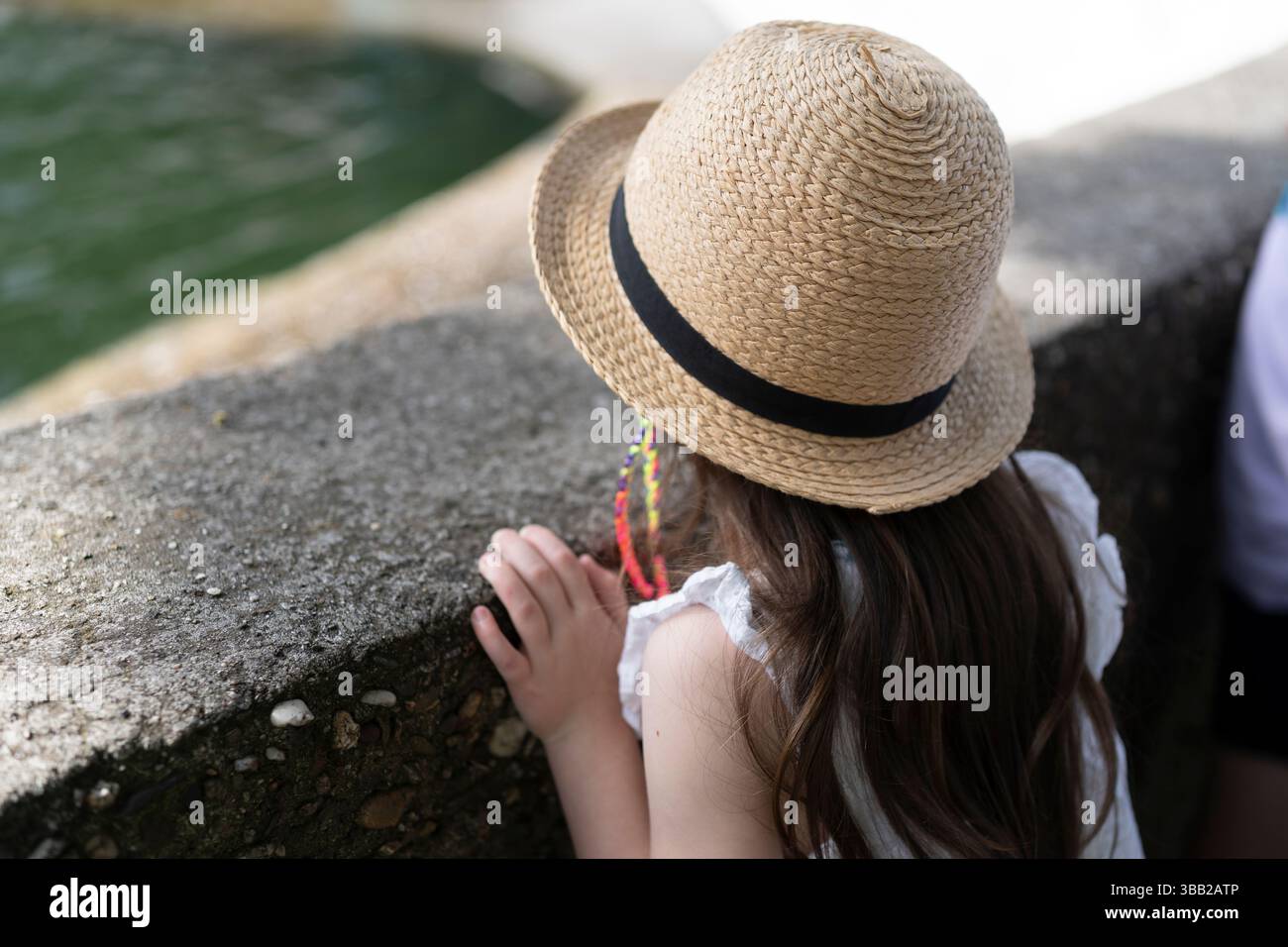 Una ragazza con un cappello di paglia si appoggia su un vetro trasparente che guarda in lontananza. Vista posteriore. Concetto di interesse per l'infanzia Foto Stock