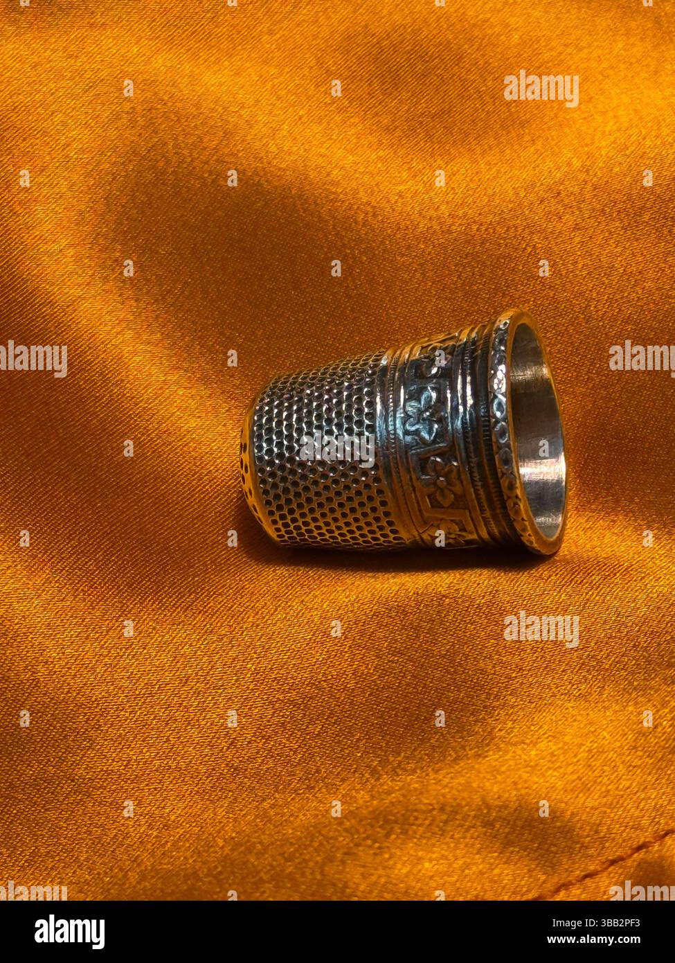 Ditale in metallo vintage su vivace tessuto in raso arancione. Primo piano di STILL Life con texture ricche e tonalità di colore calde. Ideale per concetti come cucito, cra Foto Stock