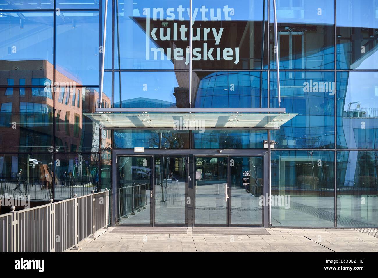 Moderno ingresso in vetro dell'Istituto di Cultura Urbana di Gdańsk con riflessi dell'edificio e un design urbano pulito Foto Stock