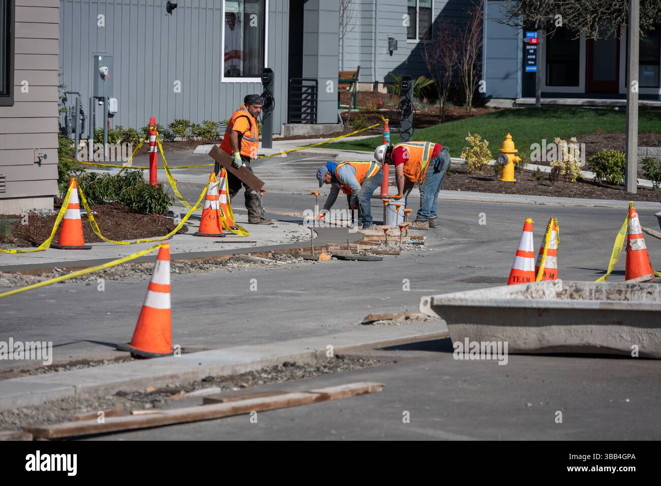 KIRKLAND, WA – APR 4, 2025: Il personale dei lavori stradali utilizza una cazzuola per spianare marciapiede e marciapiede in cemento appena versato, nuova strada abitativa della comunità, ma Foto Stock
