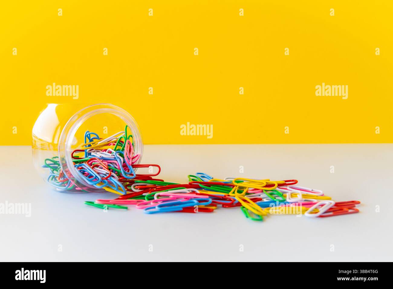 Le vivaci graffette che fuoriescono dal vaso trasparente su sfondo bianco e giallo simboleggiano le forniture creative per la scuola equilibrio visivo ufficio minimale Foto Stock Le vivaci graffette che fuoriescono dal vaso trasparente su sfondo bianco e giallo simboleggiano le forniture creative per la scuola equilibrio visivo ufficio minimale Foto Stock