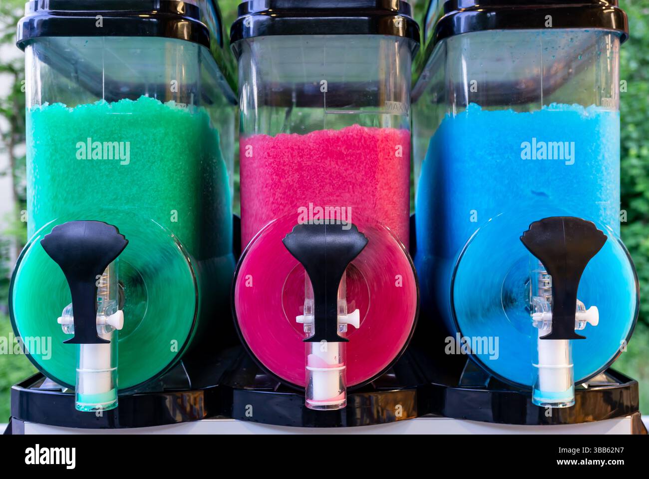 Tre contenitori colorati per bevande surgelate riempiti di ghiaccio ghiacciato in verde, rosa e blu, pronti per l'erogazione in una giornata calda. Foto Stock