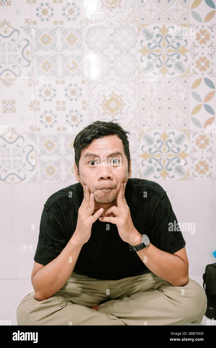 Un uomo che fa una faccia stupida, mostra emozioni giocose. Sfondo con piastrelle decorative Foto Stock