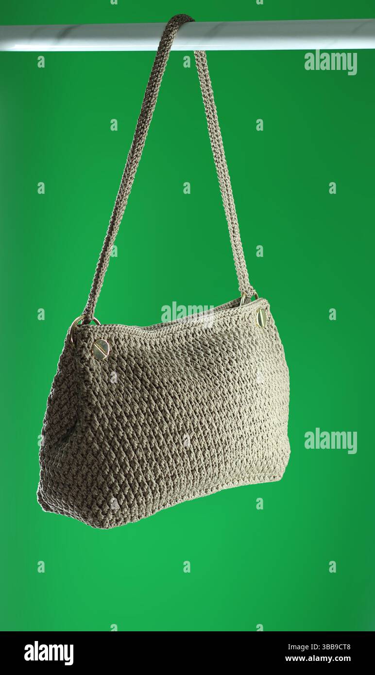 Borsa a crochet beige con motivo in marmo appeso all'appendiabiti. Isolato su sfondo verde. Foto Stock