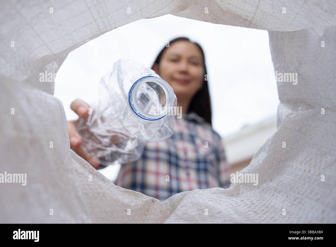 Donna asiatica che ordina una bottiglia d'acqua di plastica posta nella spazzatura per la raccolta differenziata di rifiuti da riciclare, getta diversi tipi di bottiglia in un sacchetto della spazzatura. Foto Stock
