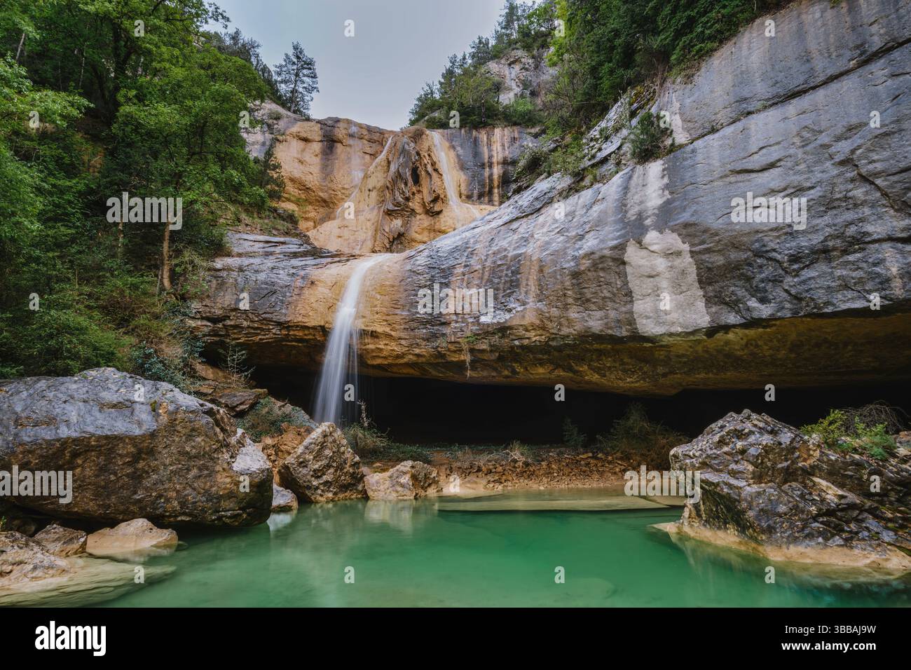 Oasi segreta di cascate sotto l'imponente sporgenza di pietra calcarea. Acque cristalline color smeraldo che formano un foro naturale per nuotare in un ambiente simile a una grotta circondato Foto Stock