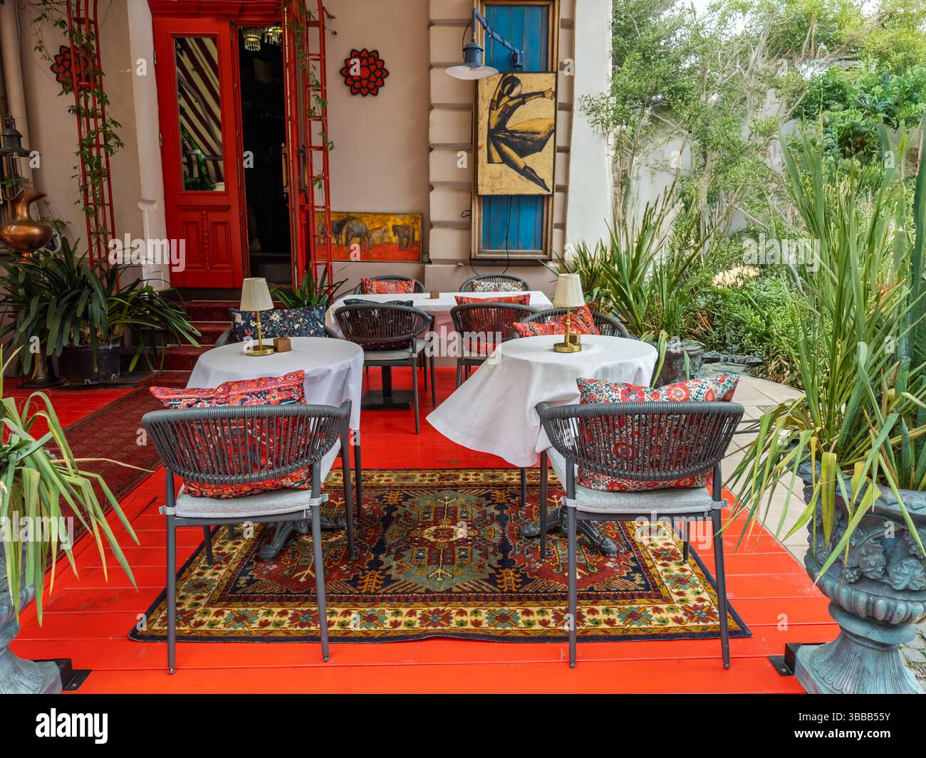 Patio del ristorante Bohemian: Pavimento rosso, tappeti etnici e tocchi artistici. Accogliente area salotto all'aperto di un ristorante con dettagli rossi e tappeti etnici. Ciao Foto Stock