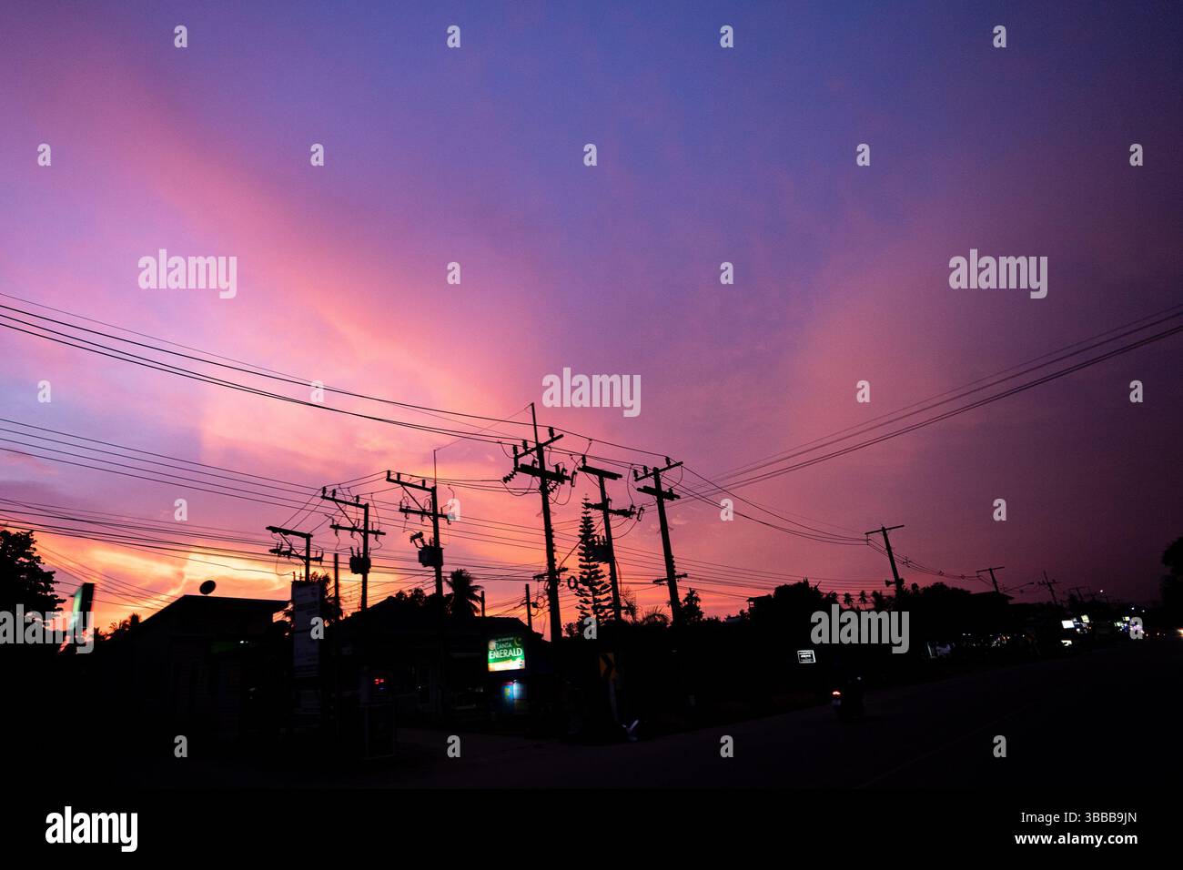 Illumina il cielo serale rosso, viola e blu con pali telegrafici ed edifici dalla silhouette Foto Stock