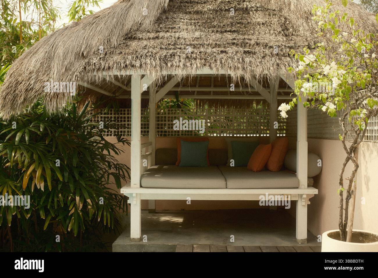 Un gazebo tropicale con tetto in paglia arredato con un letto da giorno imbottito e cuscini colorati Foto Stock