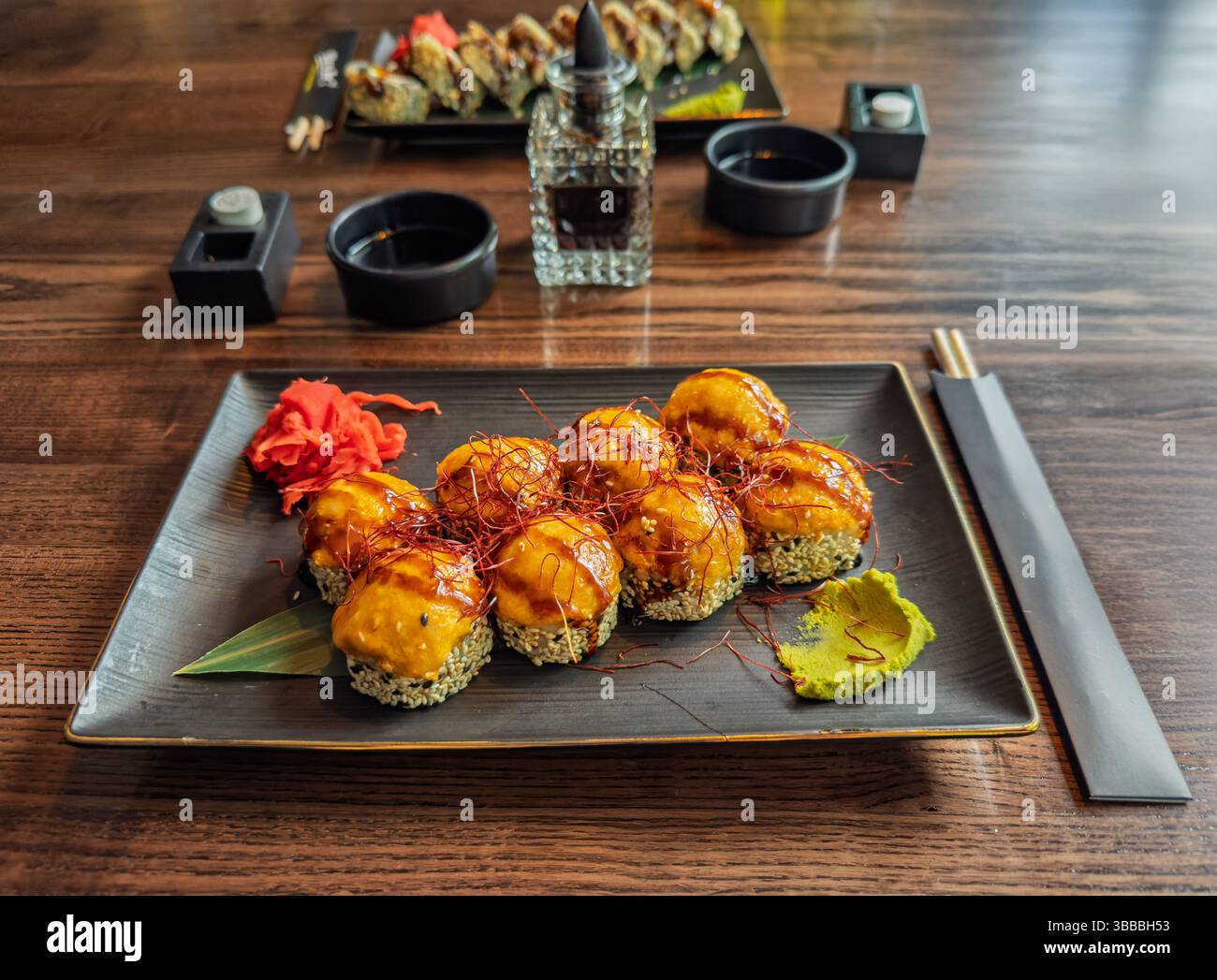 Cucina Giapponese: Delizioso sushi al forno su un tavolo di legno del ristorante. Appetitosi panini di sushi al forno con condimenti, zenzero e Wasabi. Foto Stock