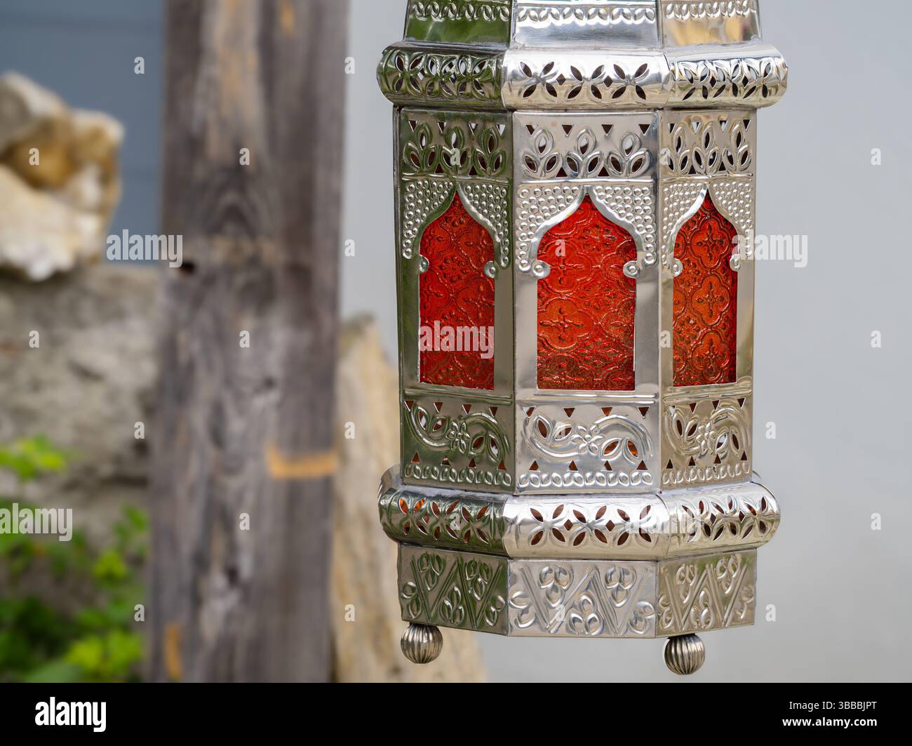 Una splendida lanterna argentata con motivi intricati e un inserto in vetro rosso brillante, appeso su uno sfondo neutro. Foto Stock