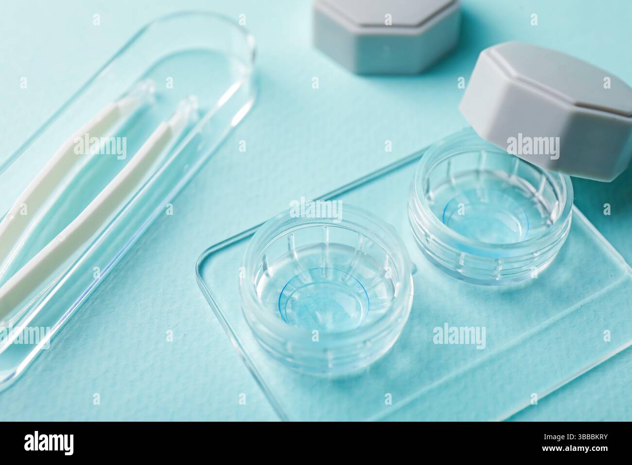 Lenti a contatto in custodia e pinzette su sfondo turchese chiaro, primo piano Foto Stock