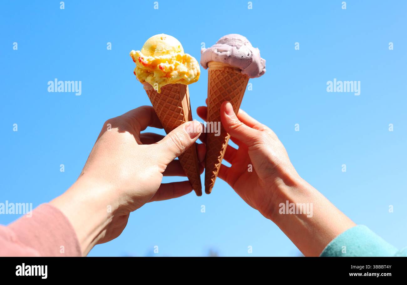 due mani che reggono due coni gelato su sfondo blu. concetto di amicizia, gioia, felicità Foto Stock