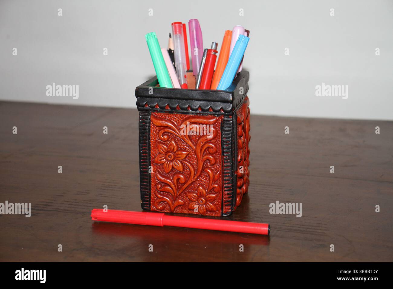 Un portapenne di colore rosso regge varie penne su una superficie in legno. Foto Stock