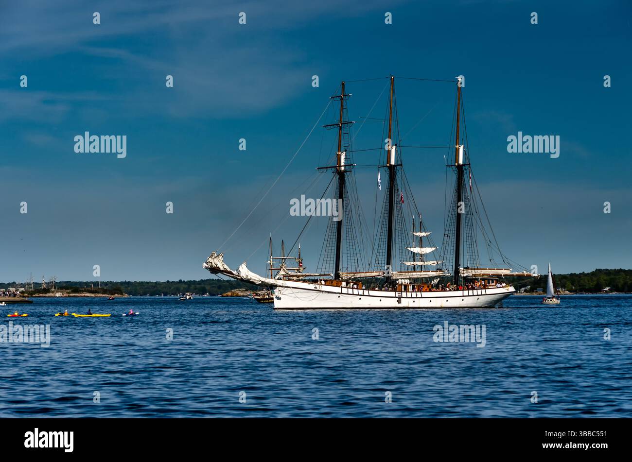 Nave White Tall ancorata nel fiume St. Lawrence, circondata da piccole barche, sotto un cielo blu. Foto Stock
