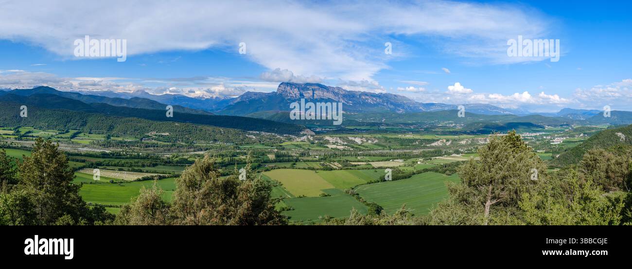 Ampia valle rurale con motivi geometrici di verdi campi agricoli sotto l'imponente catena montuosa e il cielo azzurro nuvoloso. Natura mozzafiato l Foto Stock